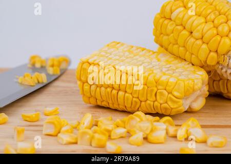 Sweet corn kernels are cut from the cob on a wooden cutting board with a knife. Using corn kernels in cooking to make delicious desserts. Stock Photo