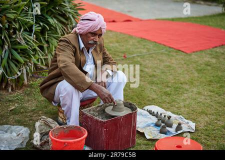 New Delhi, India - 10.12.2022 - Old indian sikh man in pink pagri headwear, white pants and brown jacket makes pottery items from clay, old potter cre Stock Photo