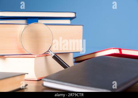 Stack book with magnifying glass on wooden desk in information library of school or university, concept for education, reading, study, copy space on b Stock Photo