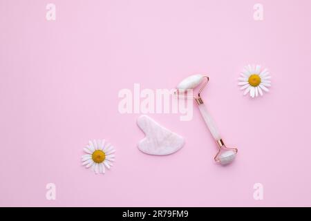 Quartz facial roller on pink background, top view. Gua sha massager from natural jade and rose stone. Face massage tool. Skin care, treatment concept. Stock Photo
