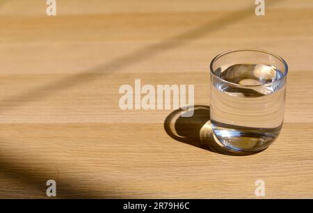 A glass of water on top of wooden table. The glass with fresh water on the wood table and sunlight. Stock Photo