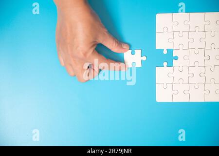 Close up hand holding and playing jigsaw game incomplete. White part of jigsaw puzzle pieces on blue background. concepts of problem solving, business Stock Photo
