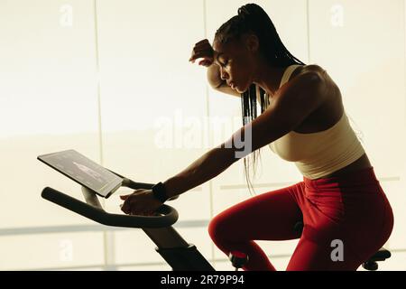 Young black woman sweating it out while working out with a cycling app. With her tablet nearby, she follows the online workout routine, pushing hersel Stock Photo