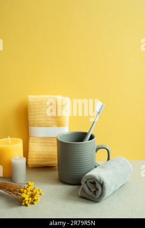 Bathroom shower towel and toothbrush, cup, candle, dry flower on gray table. yellow background Stock Photo