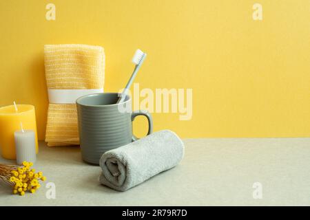 Bathroom shower towel and toothbrush, cup, candle, dry flower on gray table. yellow background Stock Photo