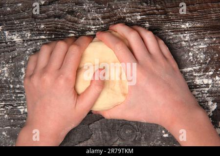 Girl kneads dough with her hands on an old brown table in a bakery. Female making yeast dough for pizza. Baking. Working prepares pastry. Kneading dou Stock Photo
