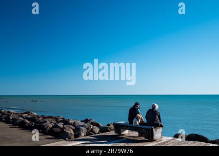 A couple with a dog sitting on a wooden pier overlooking the ocean. Stock Photo