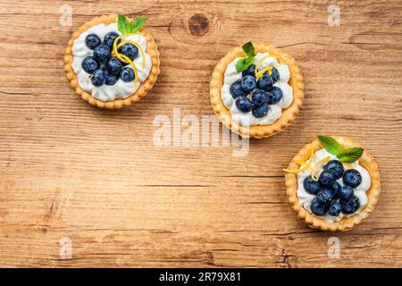 Delicious Blueberry tartlets with vanilla cream on the wooden background. Top view. Stock Photo
