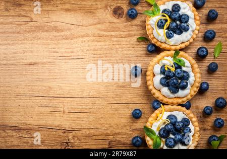 Delicious Blueberry tartlets with vanilla cream on the wooden background. Top view. Stock Photo
