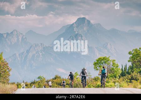 Group of cyclists riding on an asphalt road with view of mountains in the haze Stock Photo