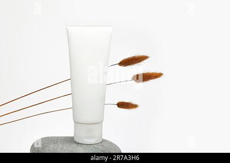 Unbranded flacon for cream, concealer, toiletry. Plastic cosmetic tube on stone and brown herbs Lagurus. Container for cosmetics product.  Eco-friendl Stock Photo