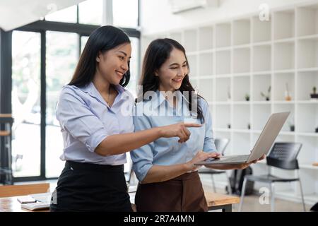 Two Asian business women working together using laptop discussing new startup project ideas. Analyze the planning and statistics of the financial and Stock Photo