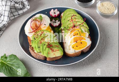 Healthy breakfast - sandwiches with avocado, egg and sesame on round plate on gray table Stock Photo