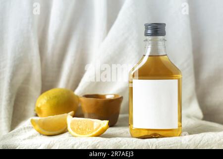 A close-up image of a bottle of lemon oil and two yellow lemons placed side-by-side on a white background Stock Photo