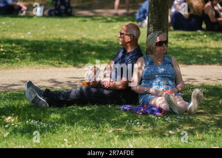 London UK. 14 June 2023 . A man and woman sitting in the shade under a tree in Saint James park London as the hot weather continues with parts of the UK  officially experiencing a heatwave due to soaring  temperatures raching 31celsius Credit: amer ghazzal/Alamy Live News Stock Photo