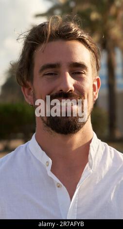 Cheerful photo of a handsome caucasian young man with long blond hair looking at camera, outdoors. Stock Photo