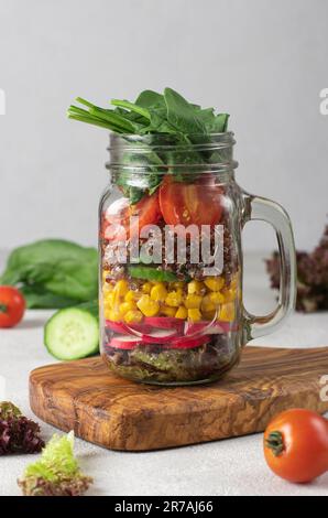 Healthy salad with quinoa, cucumbers, corn, cherry tomato, radish, spinach, lettuce and olive oil in a Mason jar Stock Photo