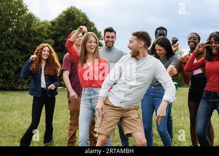 Happy group of friends dancing at music festival party outdoors - Diverse people celebrating together - Focus on center guy face Stock Photo