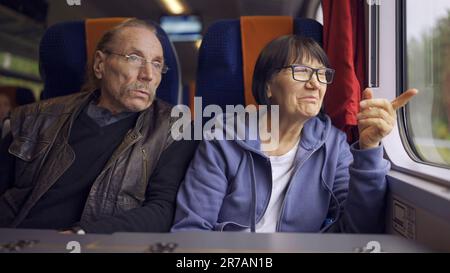 Elderly couple is riding in a train carriage and looking out the window and talking with each other Stock Photo