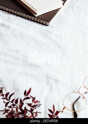 Various paper notebooks, glasses and red dry flowers on clean white bedding. Good morning concept. Copy space Stock Photo