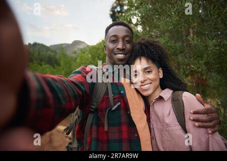 Smiling young multiethnic couple taking selfies on a hiking trail Stock Photo