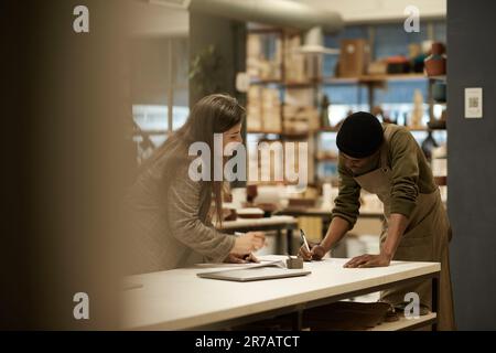Ceramics studio manager working with a colleague at a table Stock Photo