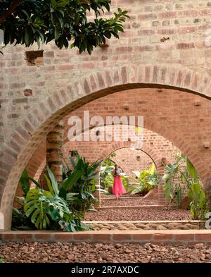 View though arches with housekeeper in colourful sari. Subteranian Ruins, Kaggalipura, Bangalore, India. Architect: A Threshold Architects, 2023. Stock Photo
