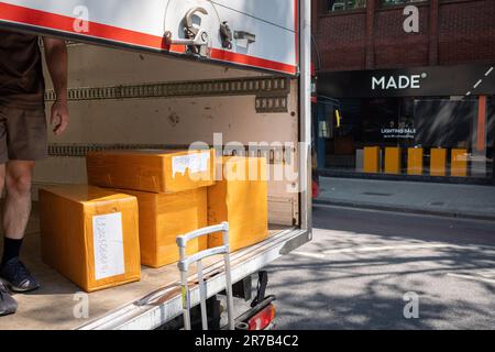 A UPS van driver unloads a stack of boxes from the rear of his vehicle for a nearby business on Charing Cross Road in Westminster, on 14th June 2023, in London, England. Stock Photo