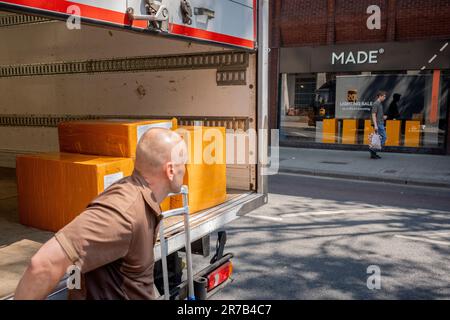 A UPS van driver unloads a stack of boxes from the rear of his vehicle for a nearby business on Charing Cross Road in Westminster, on 14th June 2023, in London, England. Stock Photo