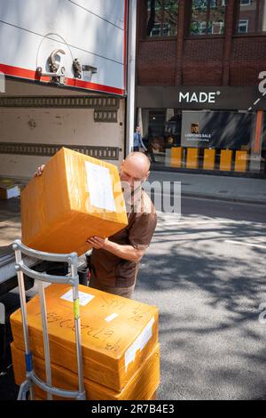 A UPS van driver unloads a stack of boxes from the rear of his vehicle for a nearby business on Charing Cross Road in Westminster, on 14th June 2023, in London, England. Stock Photo