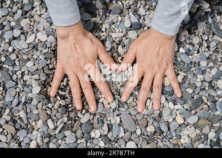 Women's hands lie on the sea pebbles. Pebble sea beach close up, dark round pebbles and gray dry pebbles, high quality photo idea for screen Stock Photo