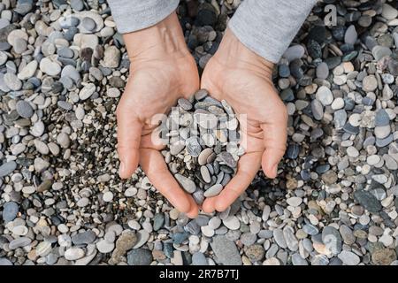 Women's hands with sea pebbles. Pebble sea beach close up, dark round pebbles and gray dry pebbles, high quality photo idea for screen Stock Photo