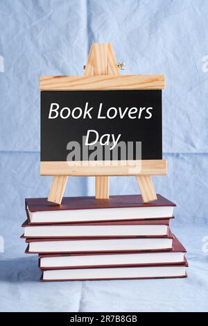 Book Lovers Day written on black board on stack of books on blue background. book holiday, education concept. Stock Photo