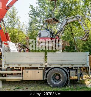 An excavator is lifted from a truck trailer with the help of a crane Stock Photo