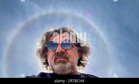 Self-portrait with smartphone, in the background the sun with halo effect, which are caused by the reflection and refraction of light on ice crystals Stock Photo