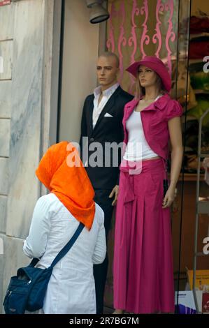Muslim woman in head scarf passes mannequins in modern attire at a Shop window Taksim, Istanbul, Turkey Stock Photo
