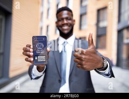 Happy black businessman in suit holding smartphone, using chatbot Stock Photo