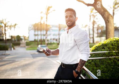 Successful happy man entrepreneur using cellphone, standing outdoors and smiling at camera, walking outside Stock Photo