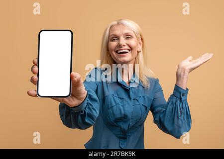 Excited pretty blonde mature woman showing smartphone with mockup Stock Photo