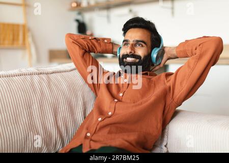Cheerful indian man listening to music in headset at home Stock Photo