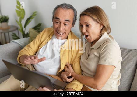 Emotional senior couple using laptop at home, aged man and woman having video call with family, living room Stock Photo