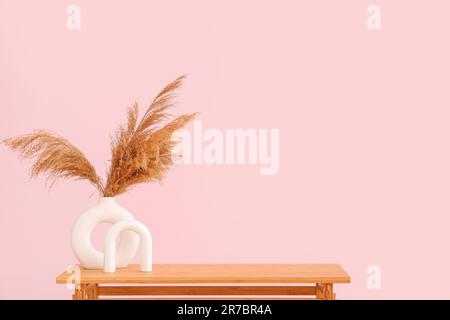 Wooden table with pampas grass in vase near pink wall Stock Photo