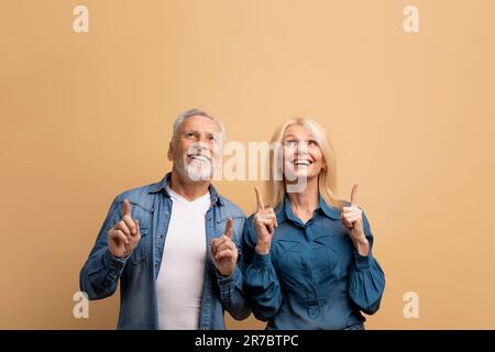Excited senior man and woman pointing up at copy space Stock Photo