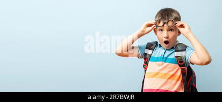 Surprised schoolboy in glasses with backpack on blue background Stock Photo