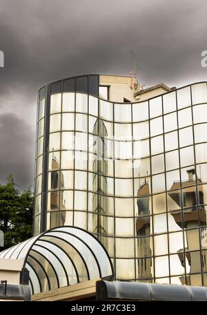 Detail of reflective glazed building in which the surrounding constructions are reflected, deformed. Unusual street view in Prato, Tuscany, Italy Stock Photo