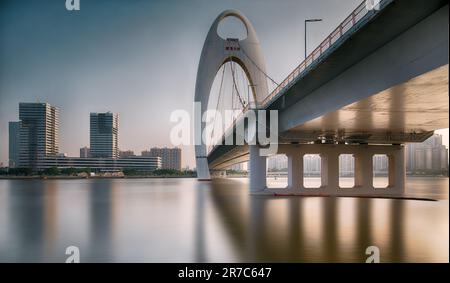 A picturesque scene of the Guangzhou bridge arching across a large body of water, with an overpass in the background, China Stock Photo