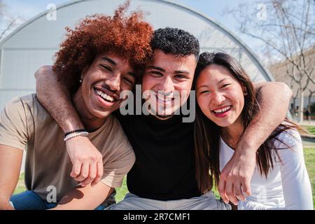 Portrait of a group of teenage students smiling and bonding at university campus. Three multiracial friends hugging and posing with friendly expression. Diverse cheerful peeople having fun together. High quality photo Stock Photo