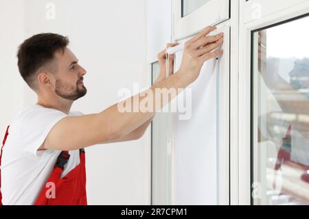 Worker in uniform installing roller window blind indoors, focus on hands Stock Photo