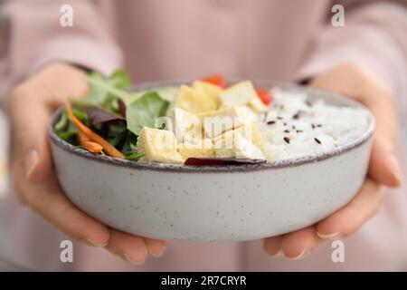 Woman holding delicious poke bowl with tofu, rice and greens, closeup Stock Photo