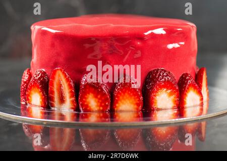 Beautiful heart-shaped moist mud cake with a ganache coating, red mirror glaze, and a fresh strawberry border. Stock Photo